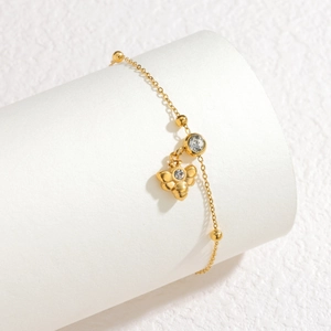Detalle de pulsera de abeja dorada con cristales y cuentas pequeñas en fondo blanco