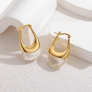 Modern U-shaped gold earrings with transparent glass beads on a white marble background