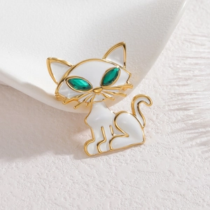 Détail de la broche chat en émail blanc avec yeux en gemme verte et contour en métal doré