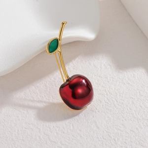 Détail d'une élégante broche cerise avec fruit en résine rouge et feuille dorée