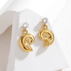 Close-up of golden nautilus shell earrings with sparkling zircon on white geometric stones