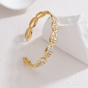 Elegant gold stainless steel cowrie shell bangle with white enamel inlay on a stone stand