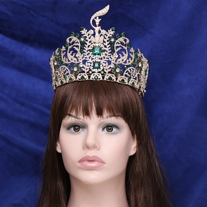 Elaborate gold pageant crown with emerald green stones and sparkling rhinestones on blue velvet