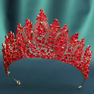 Detail view of large baroque gold bridal crown with red faceted crystals on green fabric