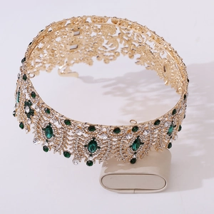 Detail of golden Baroque crown with emerald green gems and white crystal pavé on a stand