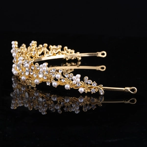 Dettaglio corona da sposa dorata con strass trasparenti e perle bianche su specchio nero