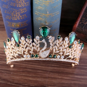 Détail de couronne cygne dorée avec strass goutte émeraude sur fond de livre vintage