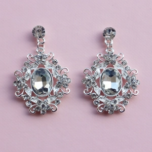 Macro detail of oval silver earrings with white crystals and Baroque style filigree pattern