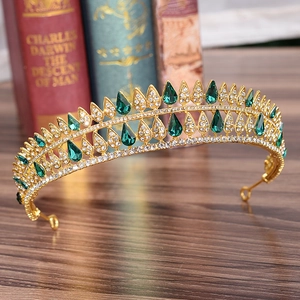 Close-up of golden Baroque crown with pear-shaped green gems and white rhinestones