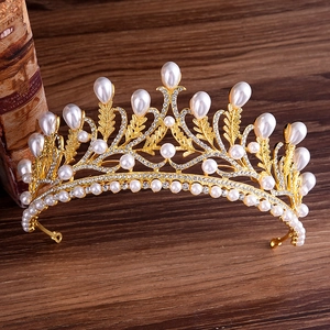 Elegant gold bridal crown with white pearls and sparkling rhinestones on wood surface
