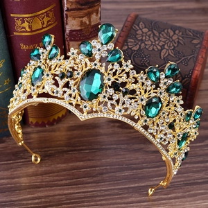Baroque gold crown with emerald green crystals and white rhinestones on dark wood