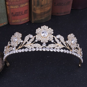 Tiara da sposa dorata con fiori di cristallo e foglie davanti a libri classici