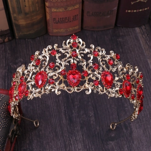 Vintage golden bridal crown with red rhinestones and intricate leaf patterns on a dark wood base