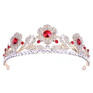 Dettaglio della tiara da sposa dorata con gemme rosse e strass scintillanti su fondo bianco