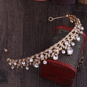 Detailed macro of golden bridal crown featuring rhinestone leaves on a vintage jewelry box