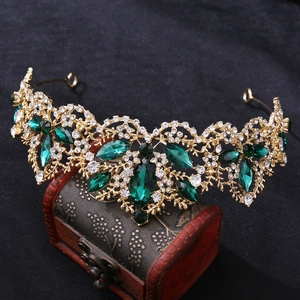 Detail of vintage golden crown with emerald green stones on a red velvet jewelry box