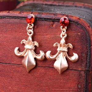 Detail view of retro fleur-de-lis earrings with red rhinestones and rose gold finish