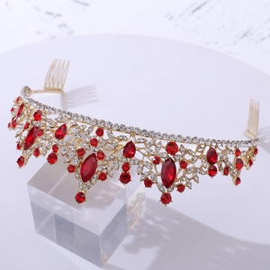 Close-up of golden bridal tiara with red crystals and hair combs on a white base