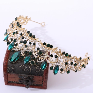 Baroque gold bridal crown with green crystals displayed on a vintage treasure chest