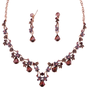Detail of vintage rose gold jewelry set with wine red crystals and floral vine design