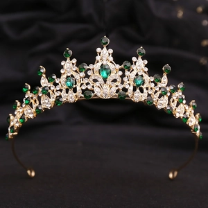 Detail view of gold bridal crown with emerald crystals on black velvet background