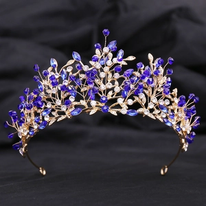 Detailed close-up of golden leaf crown with blue crystals on black fabric background