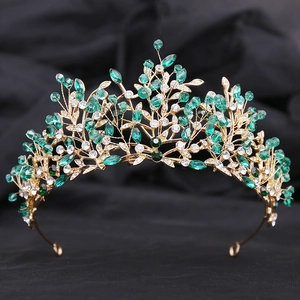 Detail of leaf-themed bridal crown with green crystals and gold wire on black background