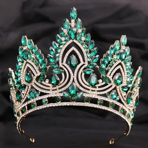 Close-up of golden crown with teardrop green crystals on dark fabric background