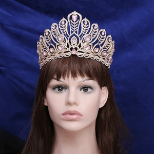 Golden peacock feather pageant crown with pink teardrop crystals on navy background