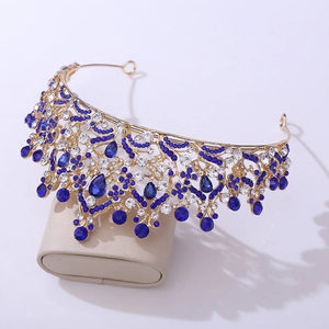 Detail view of golden crown with dark blue rhinestones on a beige display stand