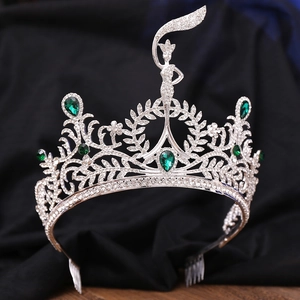 Close-up of silver crown featuring emerald green gems and elegant female relief detail