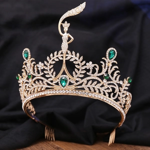 Detail of gold tiara with green emerald crystals and goddess figure on black velvet