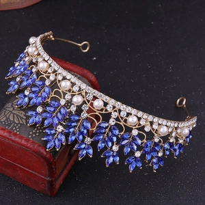 Close-up of golden leaf crown with blue marquise crystals and pearls on red wooden box