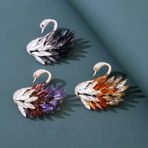 Elegant swan brooches with marquise-cut crystals in three colors on a green background