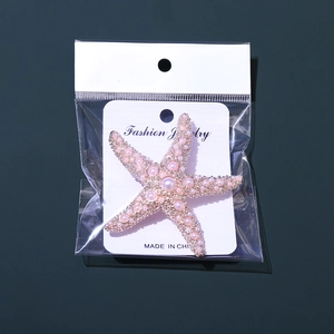 Vue détaillée d'une broche étoile de mer dorée avec perles roses sur fond vert