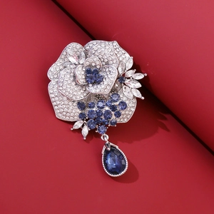 Broche de rosa brillante con pétalos plateados, cristales azules y una piedra de gota roja