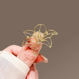 Detailed view of hollow gold lily brooch with elegant curved petals on hand