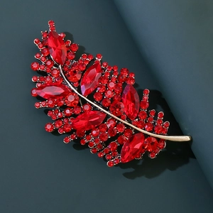 Dettaglio di una spilla a forma di foglia con cristalli rosso scuro su base dorata