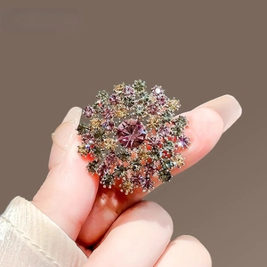 Broche de luxe fleur de pissenlit avec cristaux colorés tenue à la main sur fond sombre