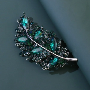 Dettaglio macro della spilla a foglia con pietre verde smeraldo taglio marquise e placcatura