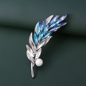 Détail d'une broche épi argentée avec cristaux bleus et perle sur fond vert foncé