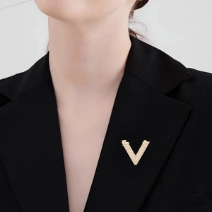 Minimalist V-shaped gold brooch with white crystals pinned on a black suit lapel