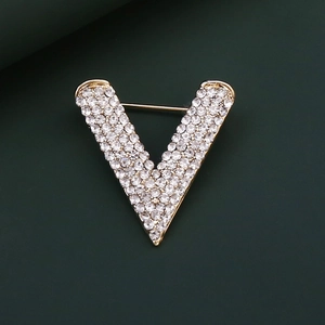 Macro shot of V-shaped gold brooch with inlaid rhinestones on dark green background