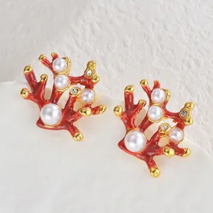 Boucles d'oreilles corail rouge élégantes avec perles et bords dorés sur fond blanc