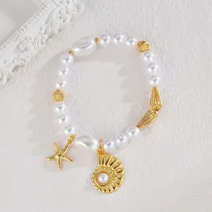 Détail du bracelet de perles avec breloques d'étoile de mer et coquillage doré sur blanc