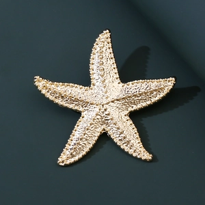 Macro shot of gold starfish brooch with granular texture on a dark teal background