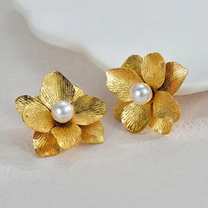 Elegante goldene Blumenohrringe mit Perle und gebürstetem Finish auf einem Teller