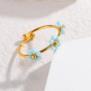 Detailaufnahme eines goldenen verstellbaren Rings mit hellblauen Perlenblumen auf Stein