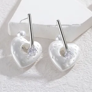 Dettaglio di orecchini a cuore in perla con barra d'argento e zircone trasparente