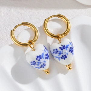 Close-up of heart-shaped blue and white porcelain earrings with golden beads and hoops